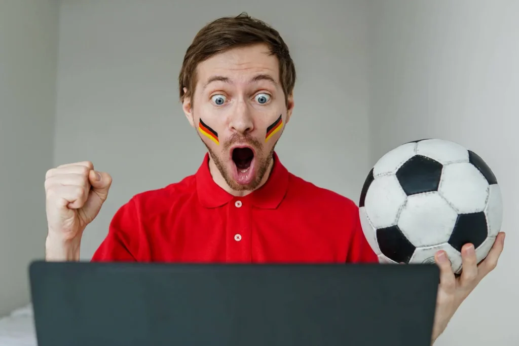 Mann am Laptop freut sich und hält einen Ball in der Hand