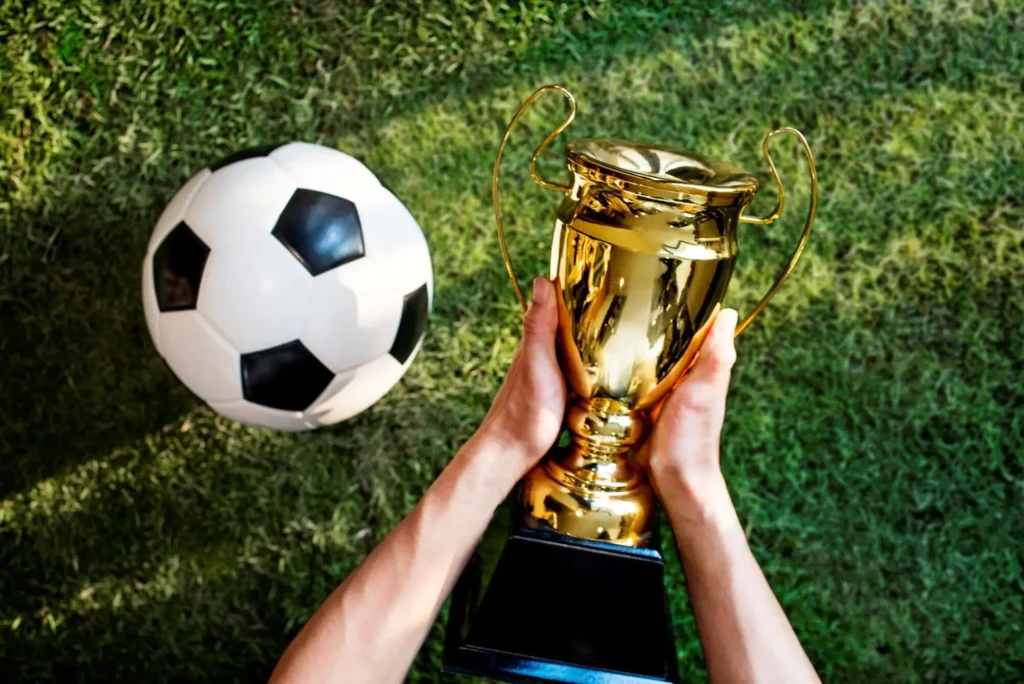 Ein Mann hält einen Pokal mit einem Ball daneben